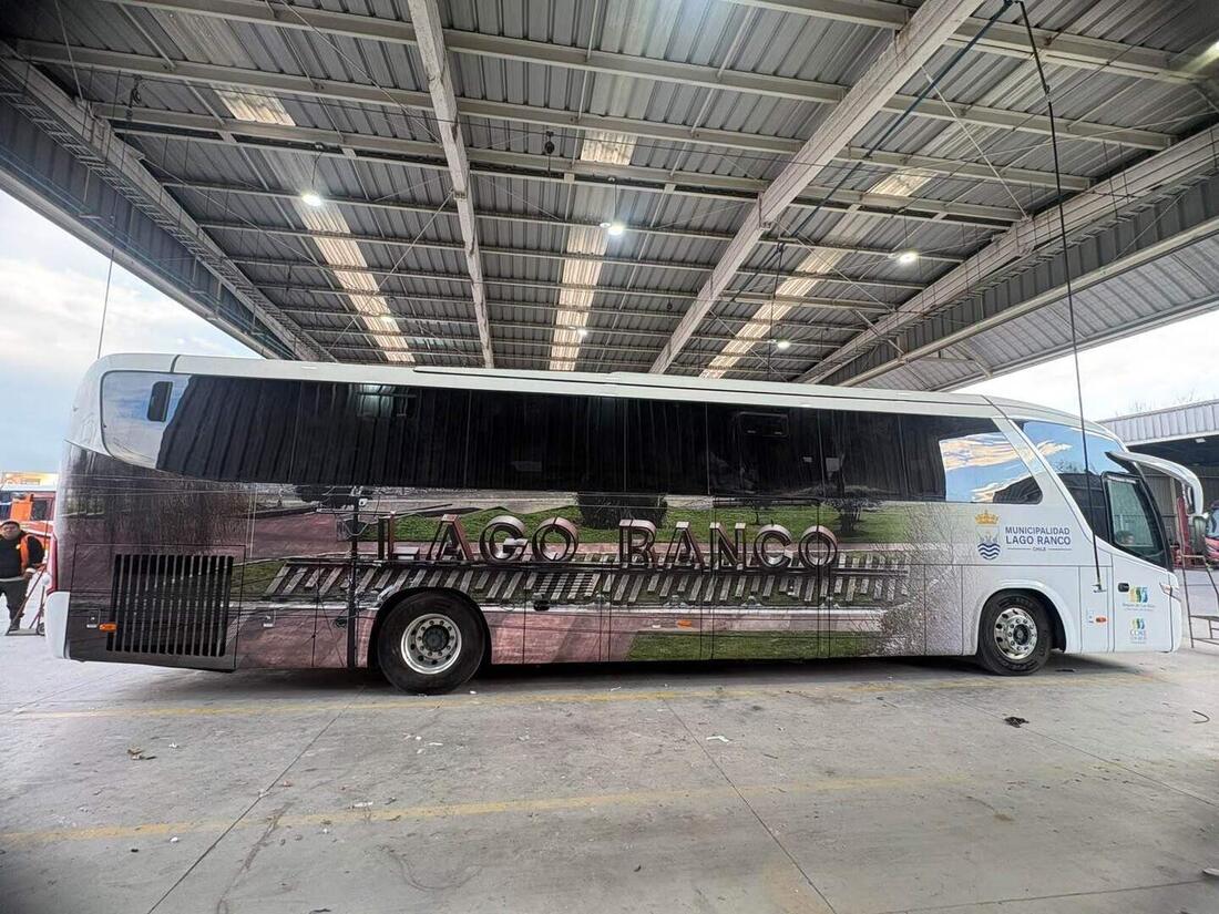 Bus de turismo con rotulación completa de paisaje a lo largo de todo el costado, en un galpón de buses