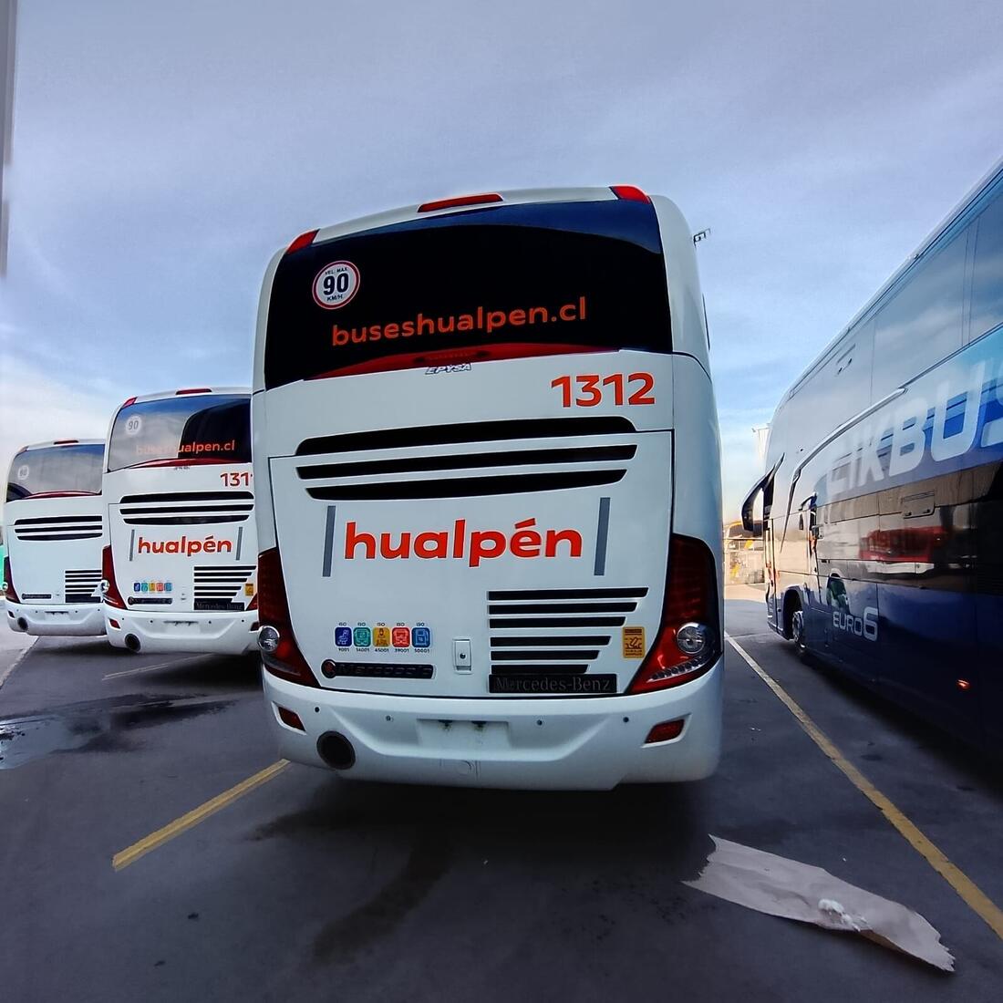 Parte trasera de un bus con gráfica corporativa, junto a otros buses de la misma flota en el patio